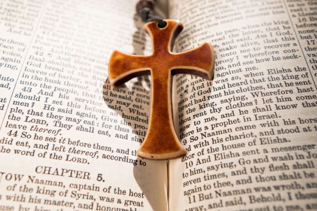 Um pingente de cruz de terracota repousa sobre as páginas abertas da Bíblia, destacando o capítulo 5 de 2 Reis, um símbolo de erudição religiosa.